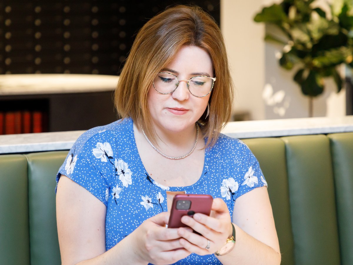 Alicia, Virtual Assistant, with brown chin length hair and a blue dress, using her phone which has a dark pink case