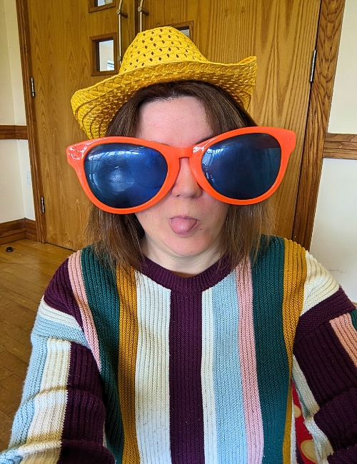 Alicia, Virtual Assistant at The Admin Den, wearing a bright yellow straw hat and giant comedy orange sunglasses, sticking her tongue out.